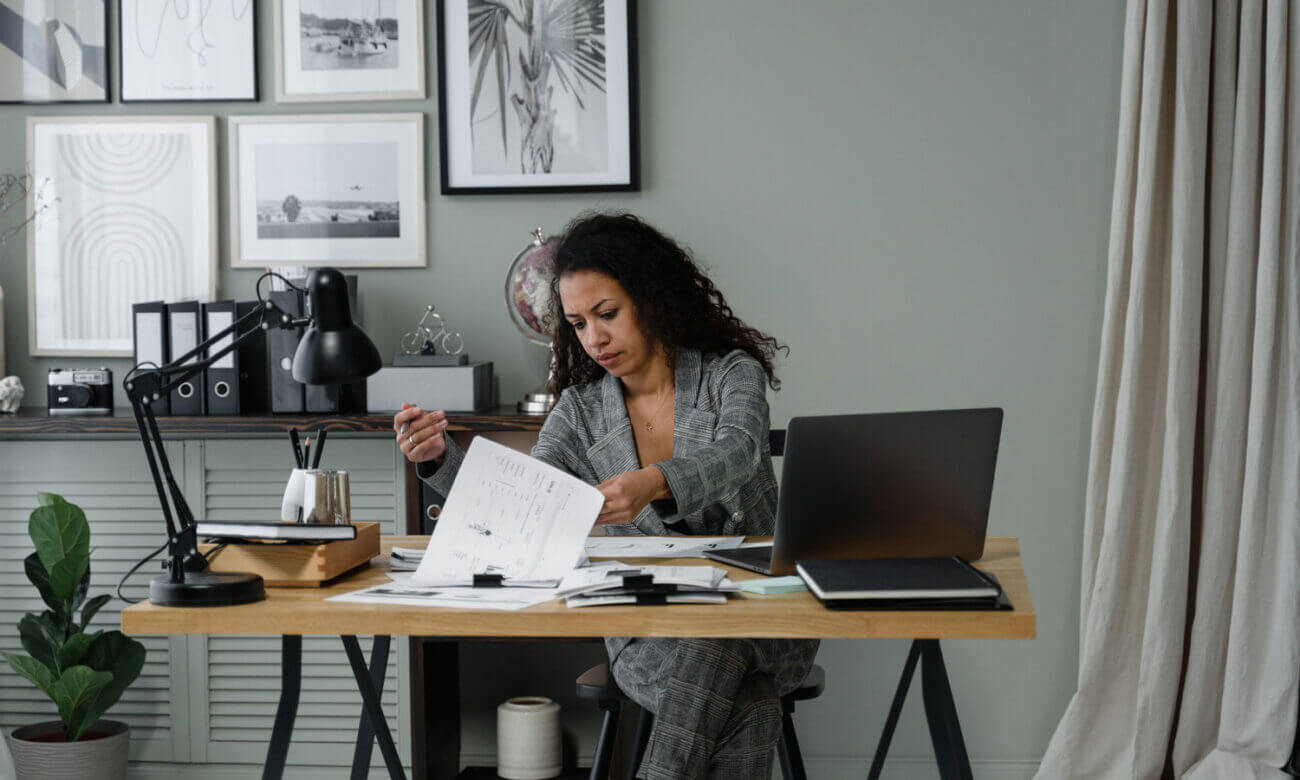 A woman is sitting at her desk at home, going through her bills to add them up.