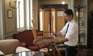 A man is closing up his restaurant, putting a chair on a table.