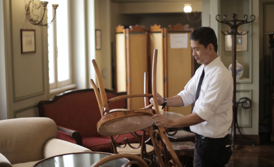 A man is closing up his restaurant, putting a chair on a table.