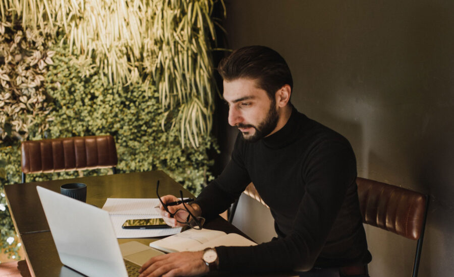 A man sits at his desk, making notes on paper as he reads about his investment accounts online