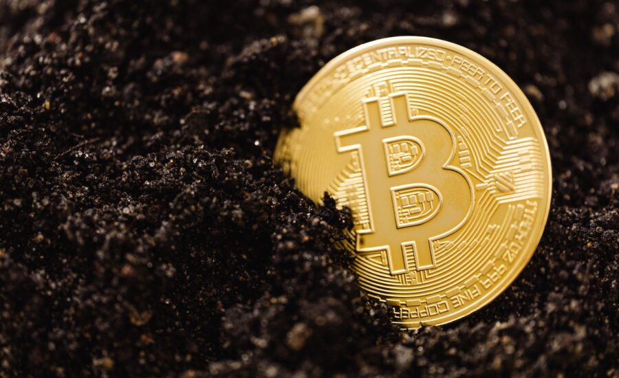 A gold coin with the bitcoin logo partly buried in soil