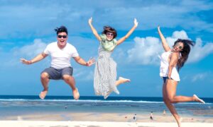 Three happy young adults jump in the air on a beach.