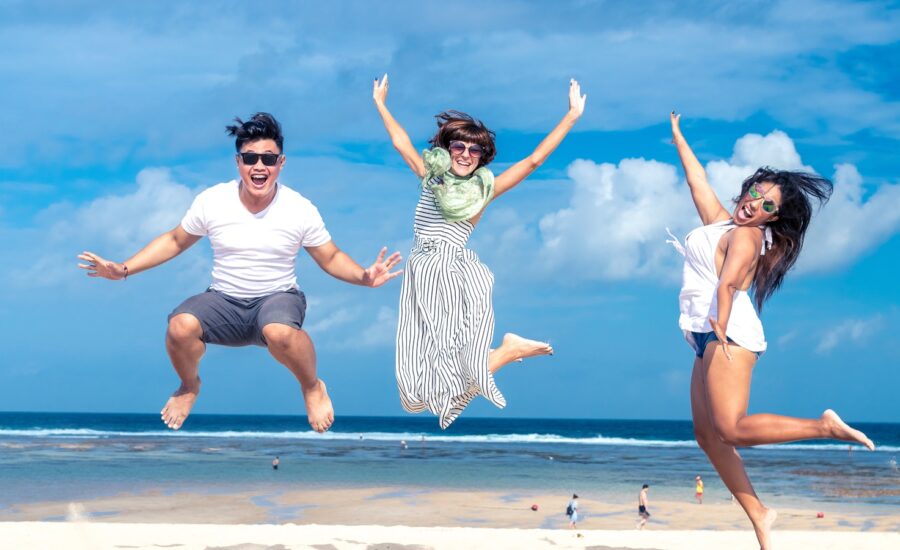 Three happy young adults jump in the air on a beach.