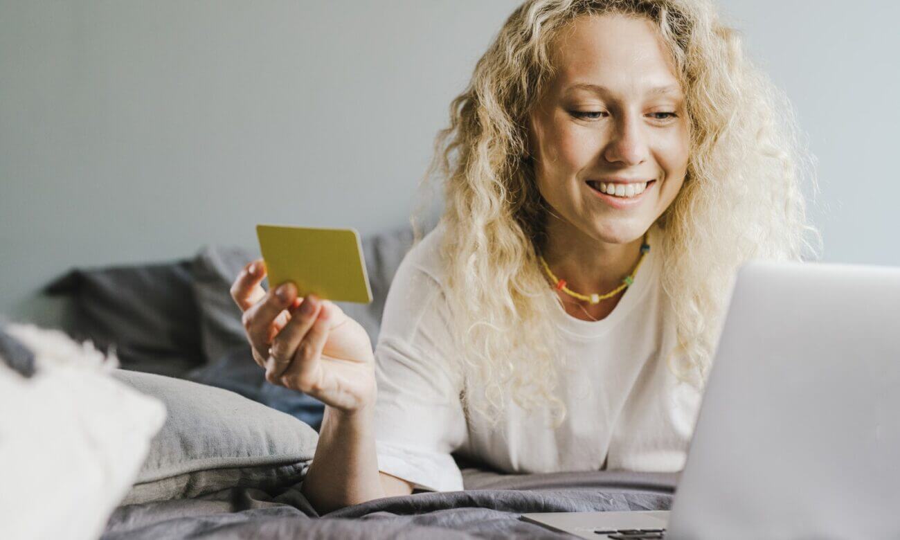 A young woman looks at her laptop and holds up a credit card