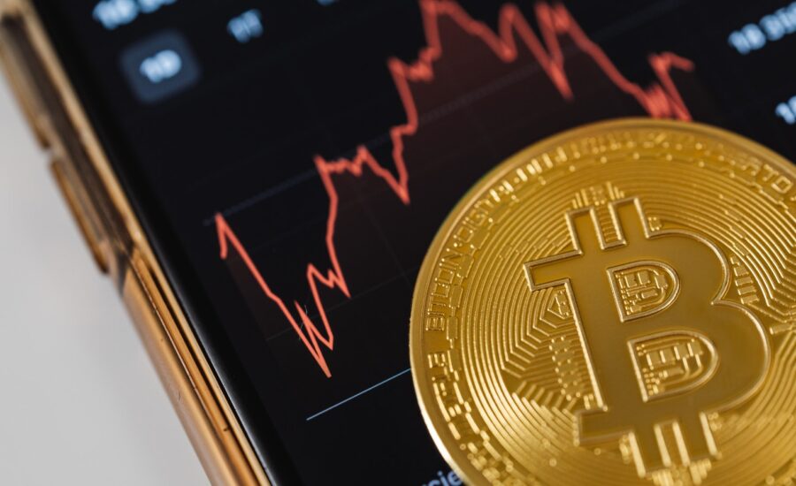 A gold coin with a bitcoin logo sits on a phone with a jagged graph