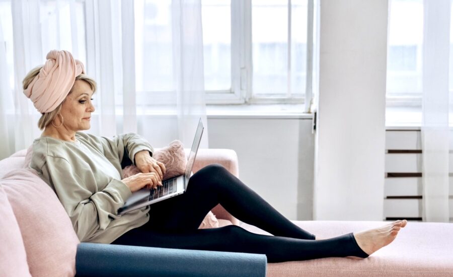 An older woman in yoga clothes sits on a sofa looking at a laptop.