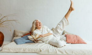 A woman is stretched out on her bed, reading a book. She has her leg kicked up in the air because she's reading about Canadian ETFs.