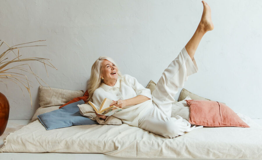 A woman is stretched out on her bed, reading a book. She has her leg kicked up in the air because she's reading about Canadian ETFs.