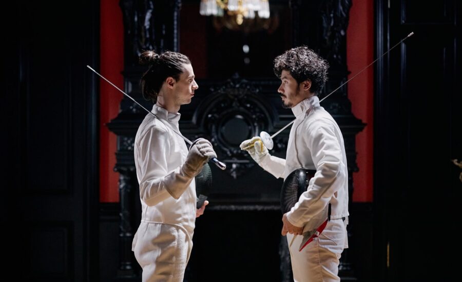 Two men in fencing gear stand facing each other.