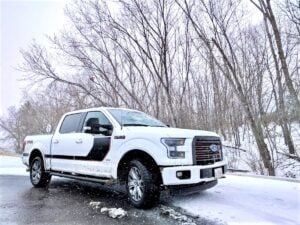 A white Ford F-150 pickup truck drives on a snowy road