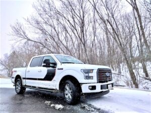 A white Ford F-150 pickup truck drives on a snowy road