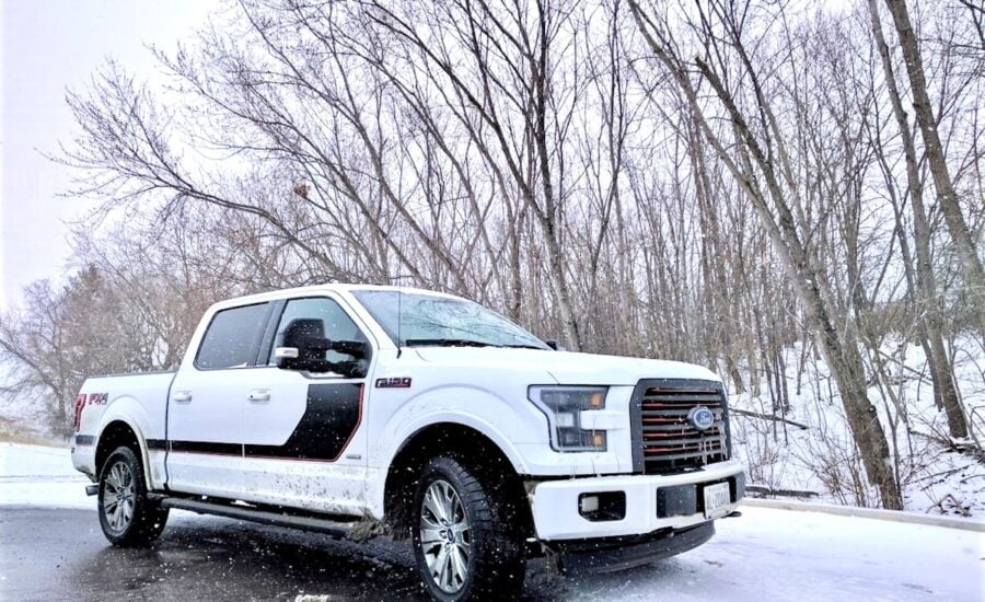 A white Ford F-150 pickup truck drives on a snowy road