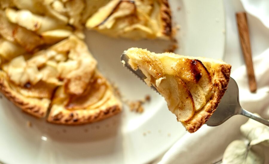 A slice of apple pie is lifted from a pie cut into eight slices