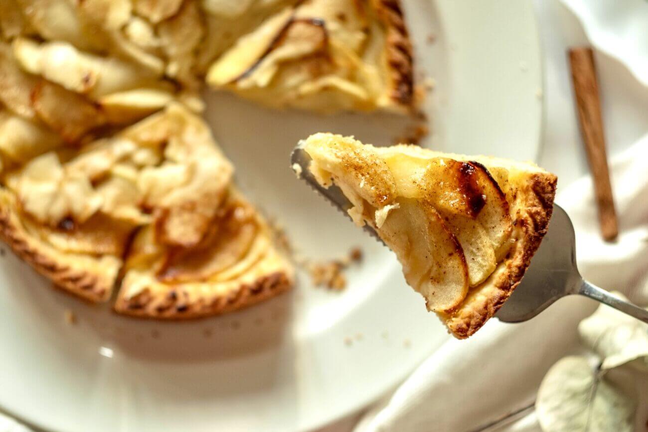 A slice of apple pie is lifted from a pie cut into eight slices