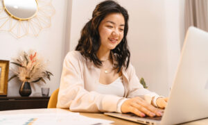 A woman is seen smiling at her laptop