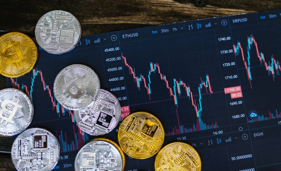 Coins with crypto logos sit on a tablet showing jagged charts