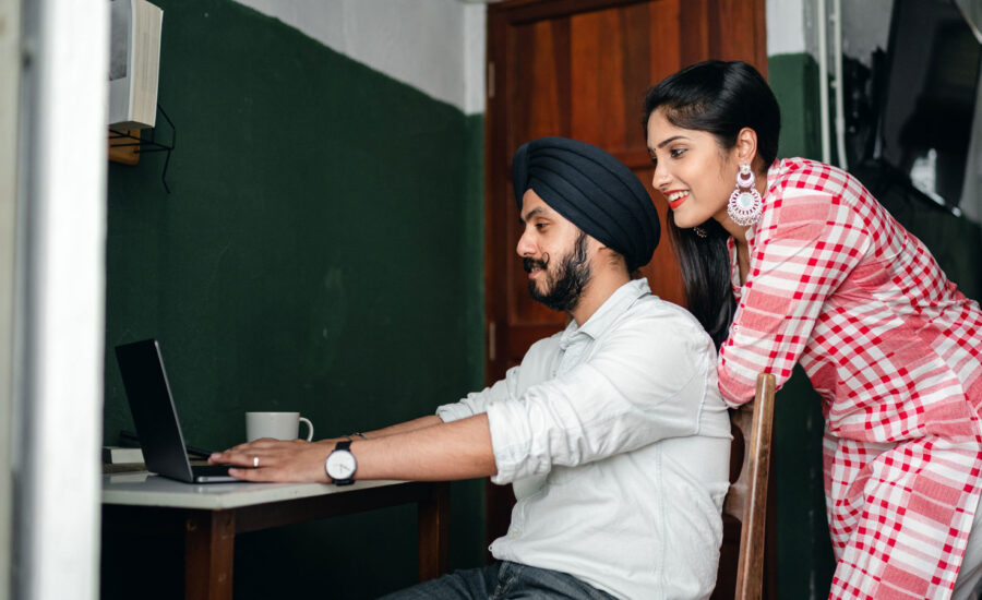 a man and a woman are sitting at a desk, smiling at what they're seeing on a laptop–as they research the value of certain stocks