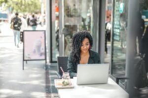 a young woman works outside a cafe on a laptop