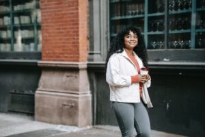 a young woman walks down a city street with a coffee