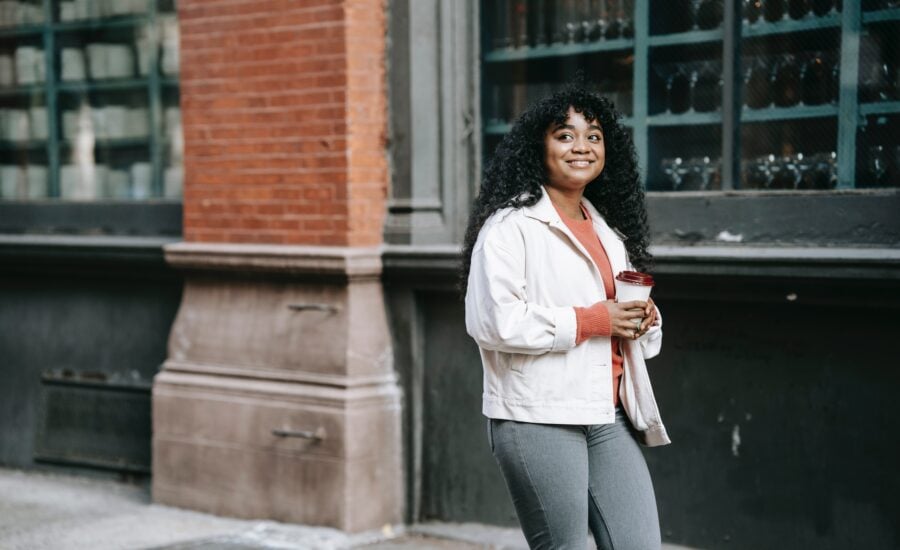 a young woman walks down a city street with a coffee