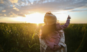 A mother holds her daughter in her arms in a field at sunset