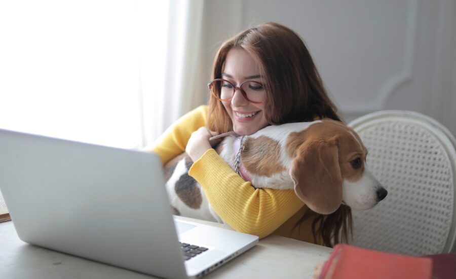 A young woman smiles at her laptop while hugging her dog