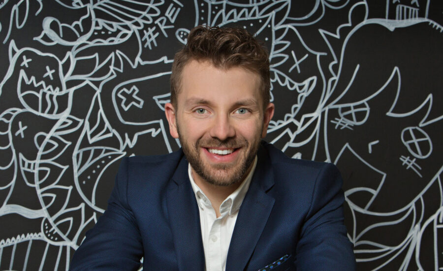 Shaun Maslyk of the Most Hated F Word stands in front of a chackboard wall