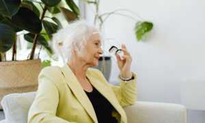 A woman in her 80s is sitting on her couch at home, removing her glasses, as she is thinking about selling her home or get a reverse mortgage.