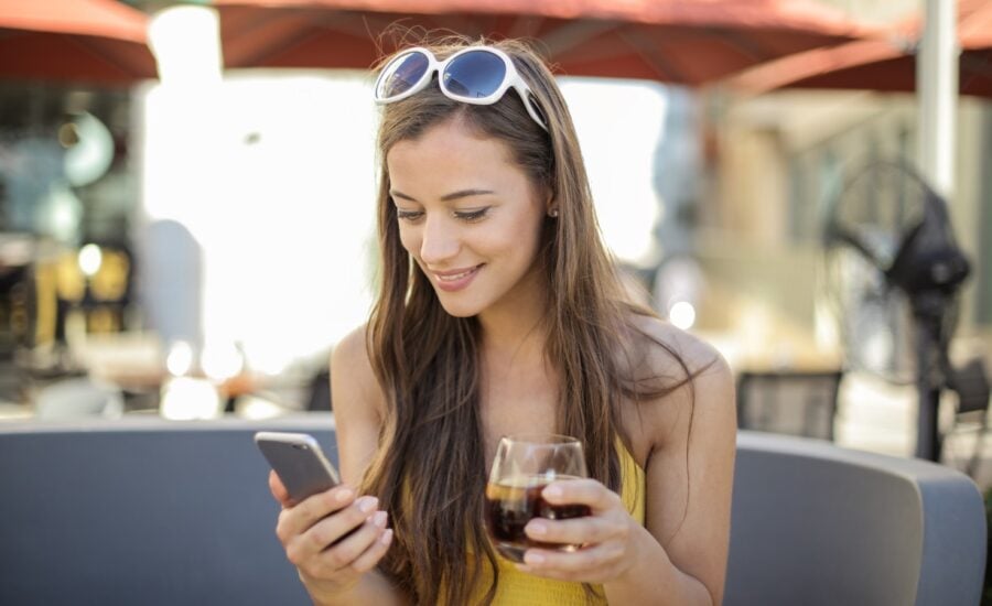 A young woman on a restaurant patio smiles at her phone