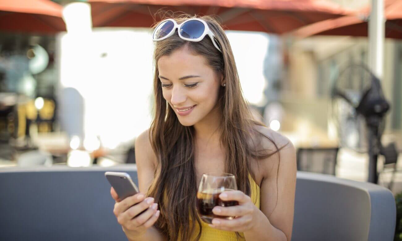 A young woman on a restaurant patio smiles at her phone