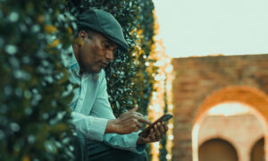 A man sits outside near hedges, contemplating transferring his home to his daughter's name