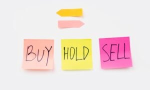 Three sticky notes saying buy, hold and sell. Above them, two arrows point in opposite directions.