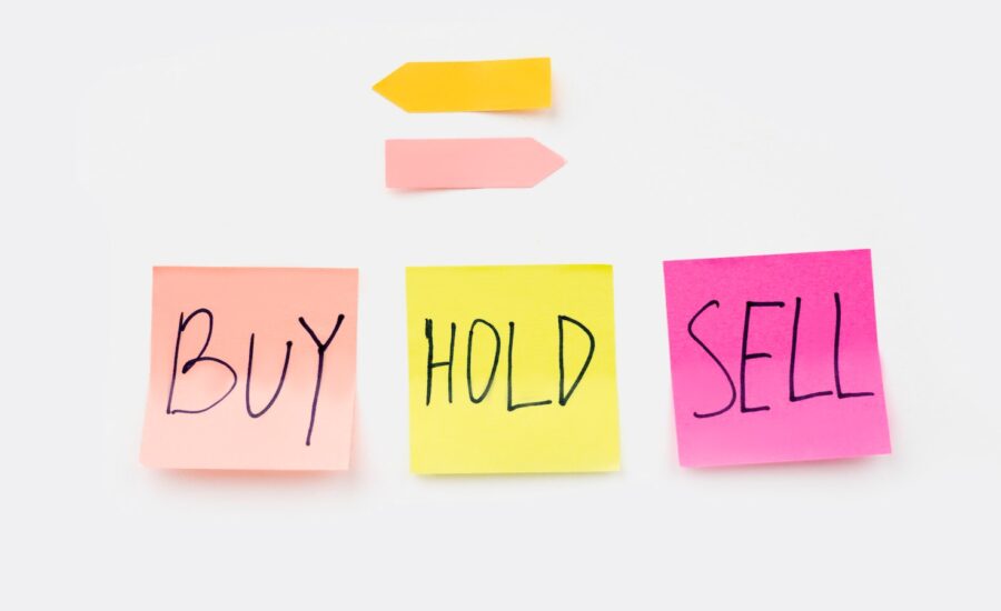 Three sticky notes saying buy, hold and sell. Above them, two arrows point in opposite directions.