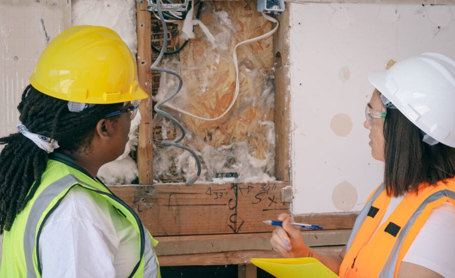 Two electricians are looking at wiring inside an exposed wall, discussing if the renovation and upgrades are tax deductible