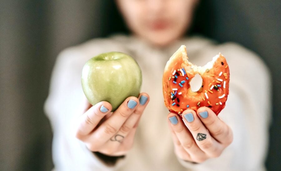 A pair of hands holding up an apple and a donut with a bite in it.