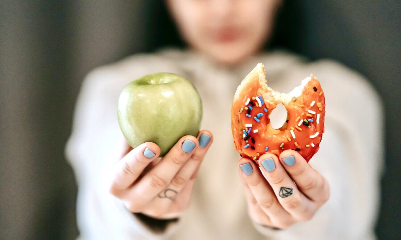 A pair of hands holding up an apple and a donut with a bite in it.