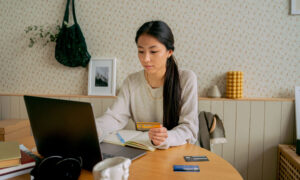 A woman sits at her computer, holding a credit card, contemplating using a line of credit to pay off her credit card debt