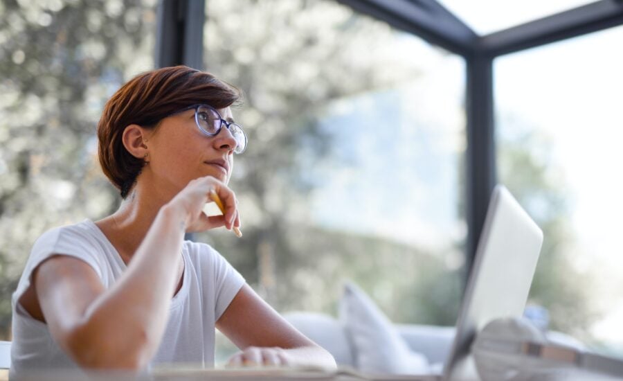 A woman sitting at her laptop gazes upward, deep in thought.