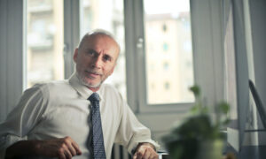 A man in the age of retirement wears a tie to symbolize that he's still working, he has an inquisitive look on his face, wondering if he should keep working and delay CPP and OAS.