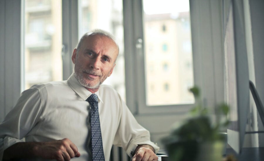 A man in the age of retirement wears a tie to symbolize that he's still working, he has an inquisitive look on his face, wondering if he should keep working and delay CPP and OAS.