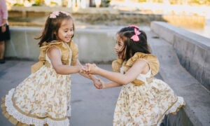 Young twin girls hold hands and dance, excited by their family's purchase of another home.