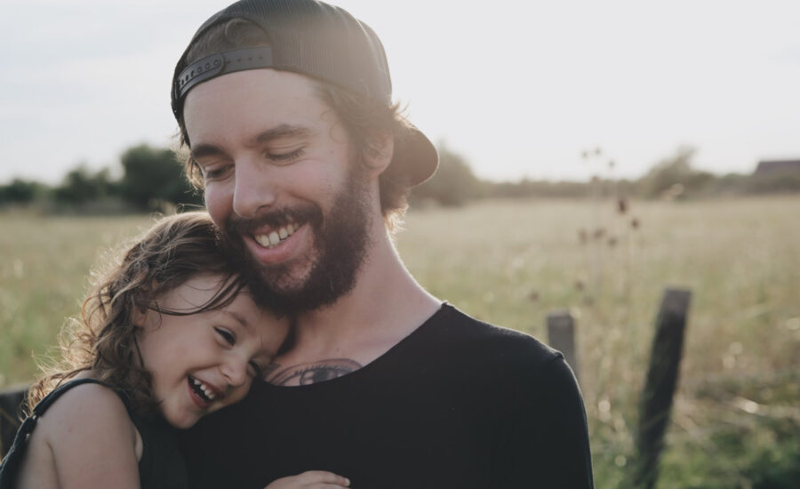 A man standing in a field considers whether he needs life insurance, while holding his young daughter in his arms