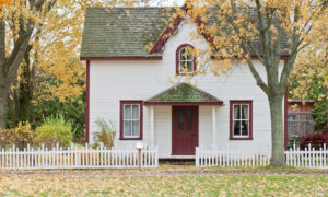 The streetview of a white house with red trim and a white picket fence in the fall