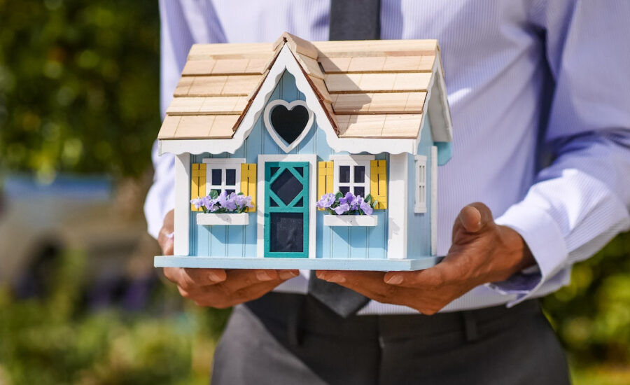 A man in a suit holds a miniature house in his hands