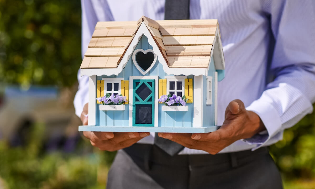 A man in a suit holds a miniature house in his hands