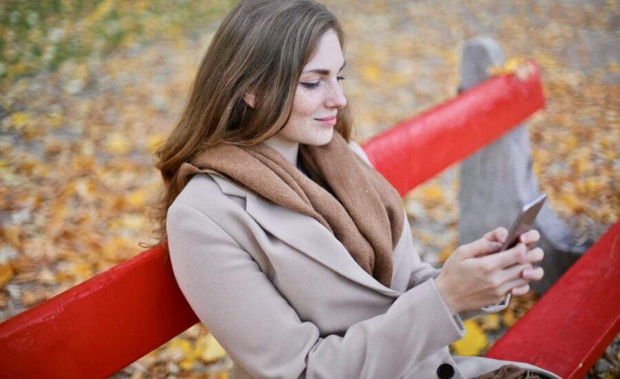 Young woman sits on a park bench smiling at her phone