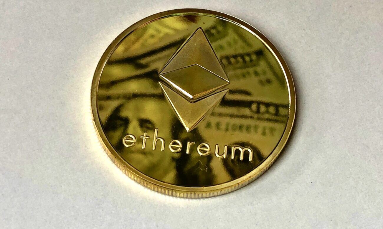 Gold coin with the Ethereum logo reflects images of American hundred-dollar bills
