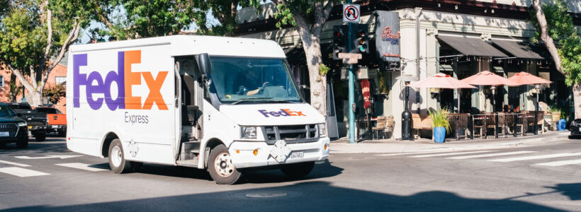A FedEx truck sits at a curb at a busy street corner, to play on the words "FedEx delivers bad news."
