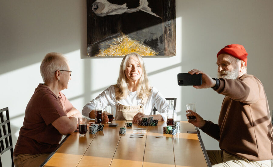 Three seniors are sitting at a table posing for a selfie photo as they play poker together. it's a symbolic photo representing how tontines work.