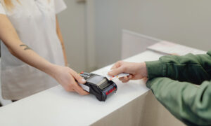 A man is tapping his credit card to pay for something, to symbolize how accustom to debt Canadians have become.